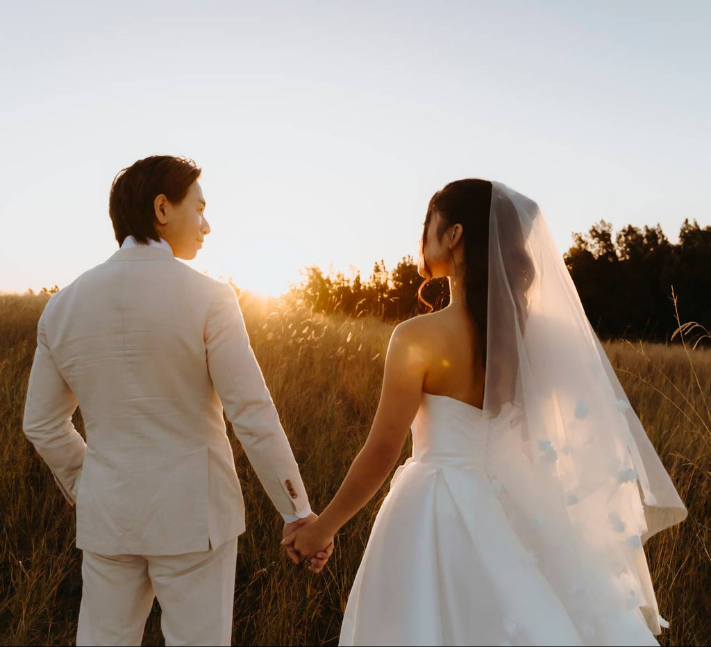 Couple in wedding attire standing in a field with sunset light